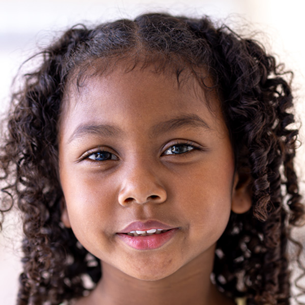 A girl with curly hair, warm smile, and dark eyes, set against a softly blurred background.