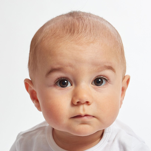 A baby with short hair gazes curiously, displaying an adorable expression with wide eyes.