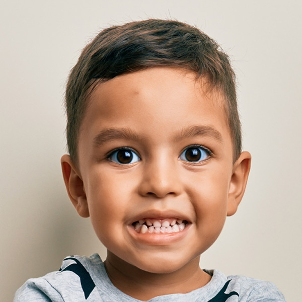 A young boy with short hair, with a beautiful eyes and a wide smile, wearing a light gray shirt.