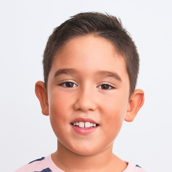 A smiling boy with short dark hair, wearing a patterned shirt against a bright background.