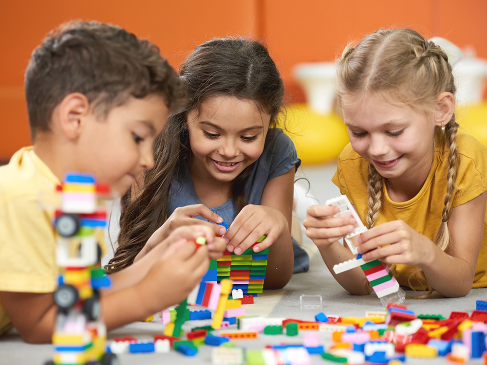 Three children happily building with colorful blocks, focused on their creative construction.