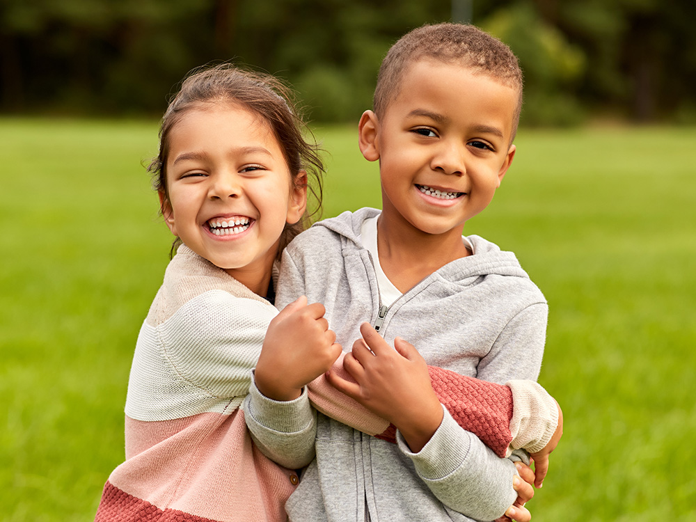 Two kids hugging themselves, smiling widely enjoying their outside playing