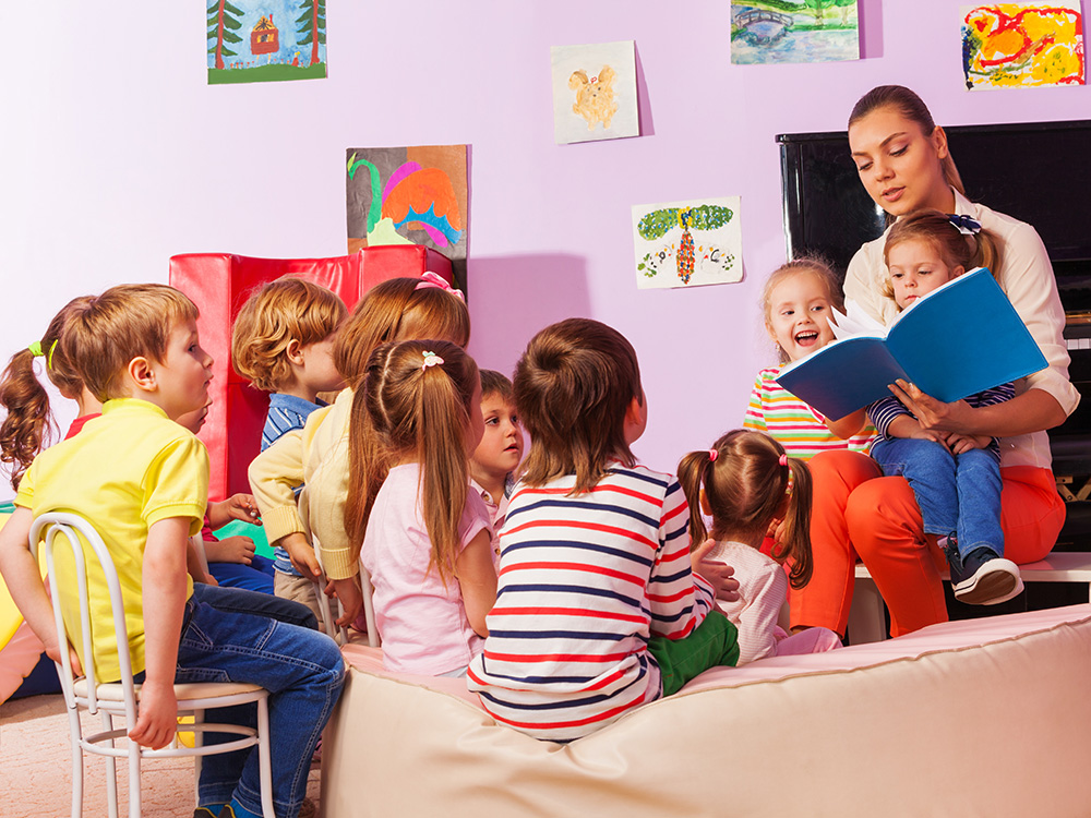 A teacher reading to a group of attentive children sitting on a couch.
