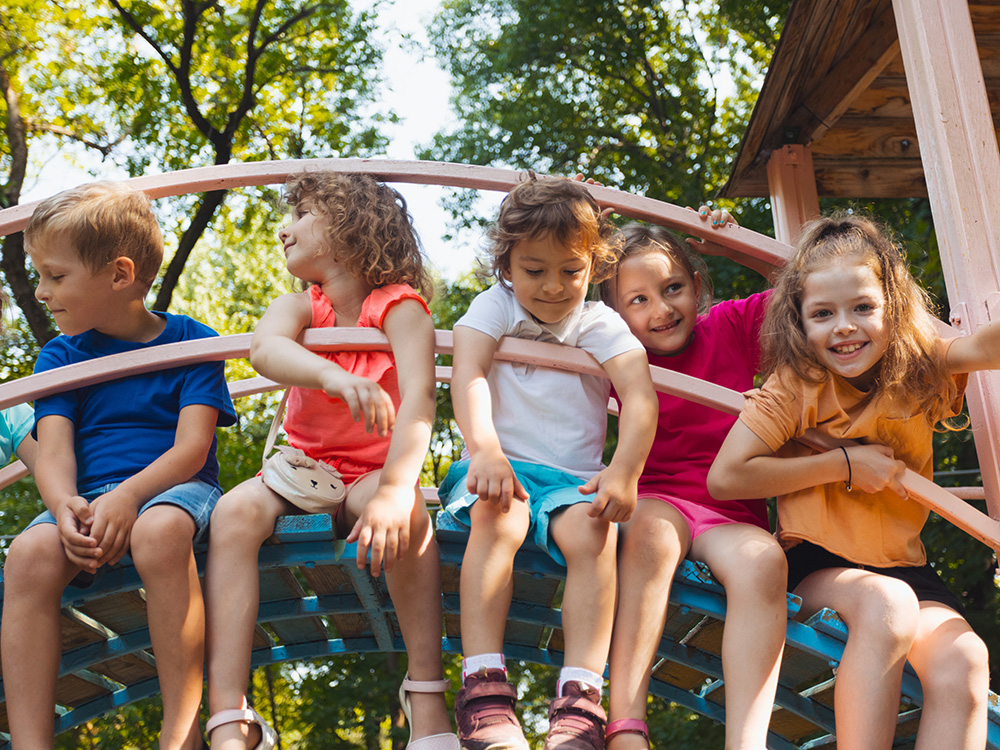 Five kids sitting on a tree house structure, laughing together and enjoying the summer outside.