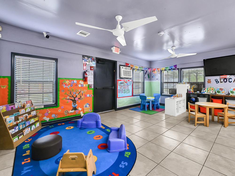 A colorful classroom with a rug, toys, and child-sized furniture, designed for learning and play.