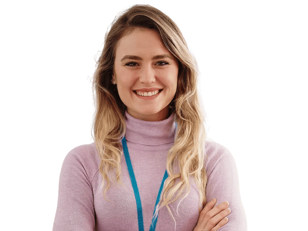 A smiling young teacher with long blonde hair, arms crossed, looking confident and friendly.