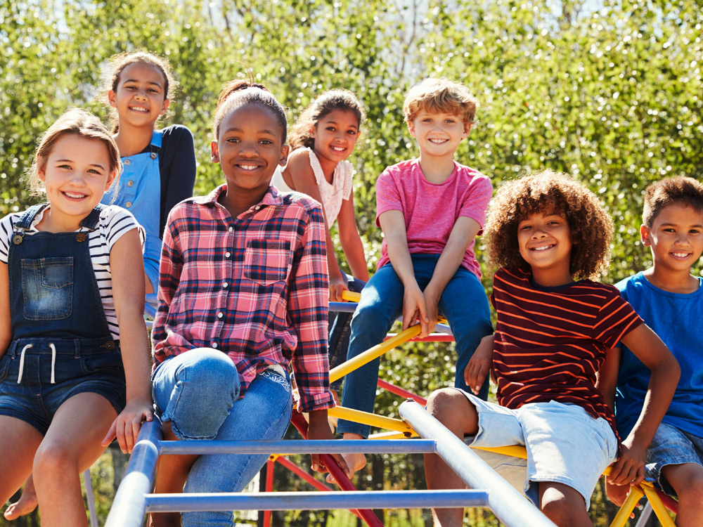A group of children sitting on playground equipment, smiling and enjoying their time outdoors.